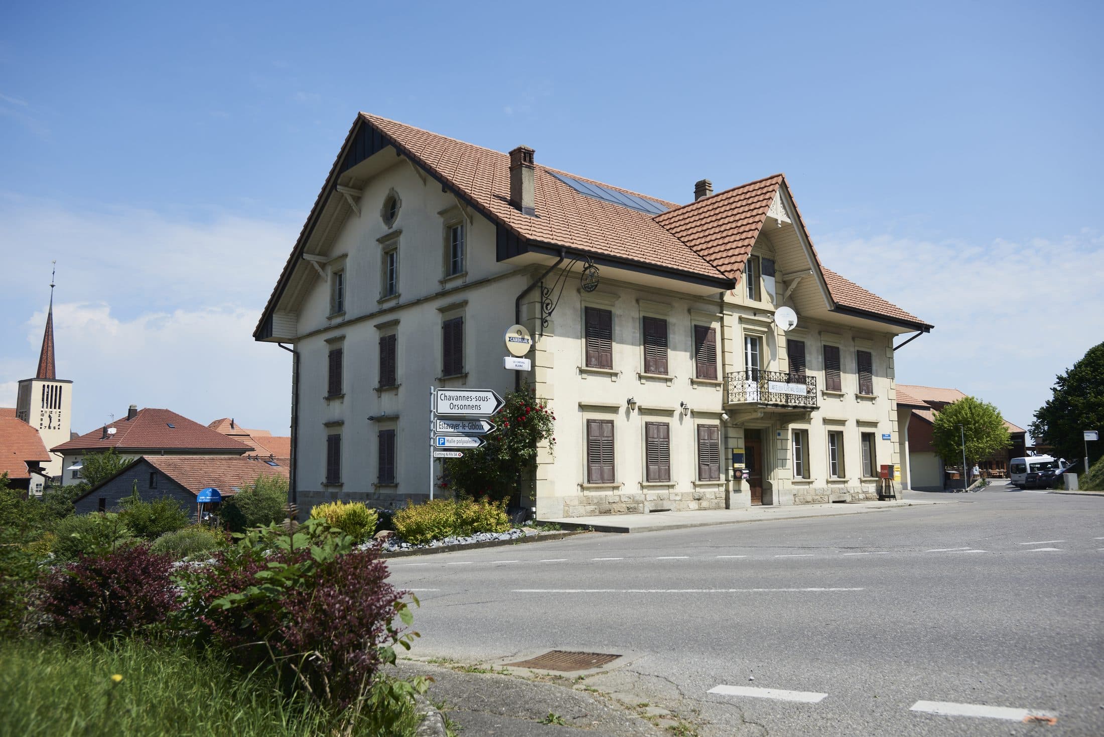 La façade de l'Auberge du Cheval Blanc à Orsonnens, sous le soleil, l'église du village à l'arrière-plan